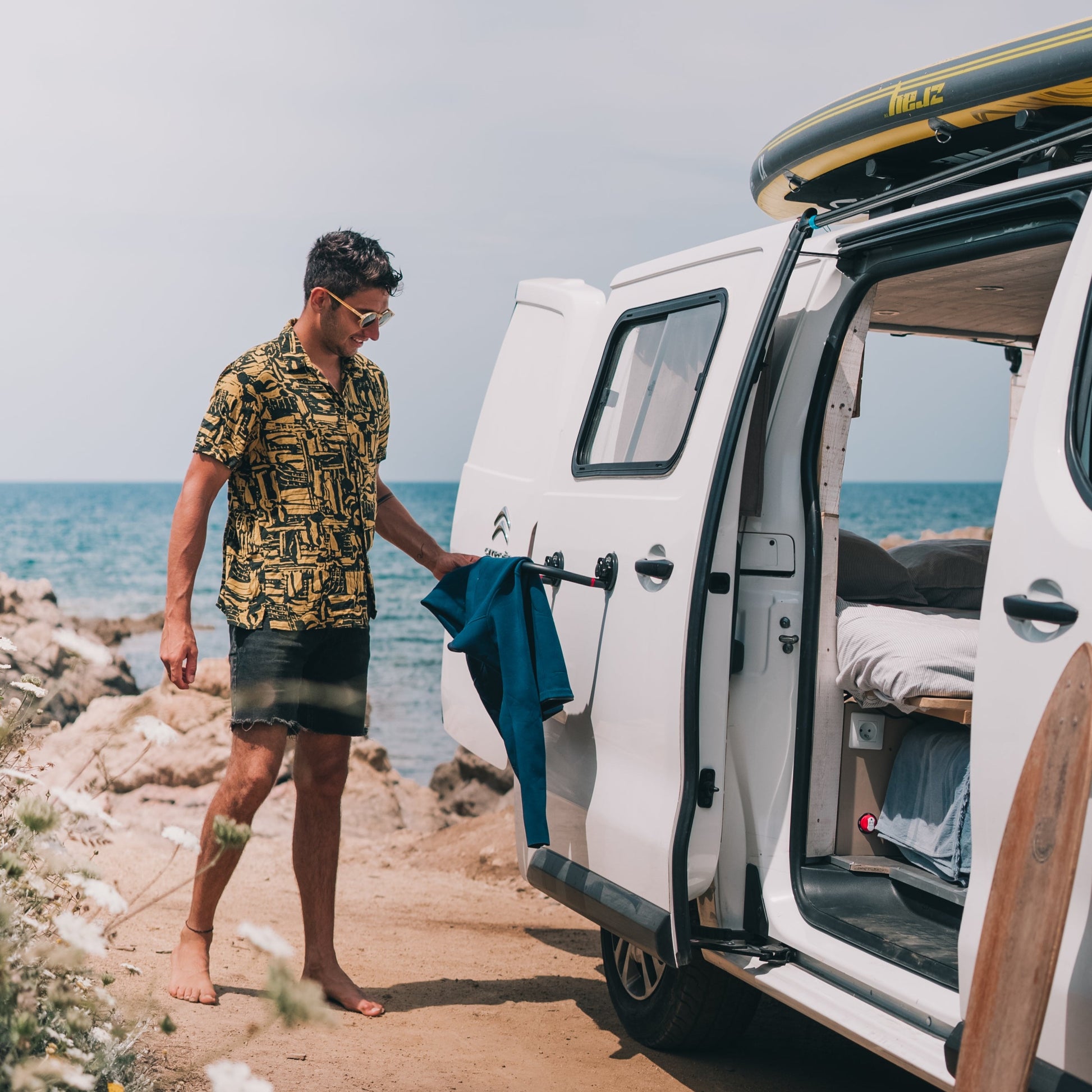 Surfeur fait sécher sa combinaison sur un séchoir Godry Hanger ventousé sur son van devant le spot